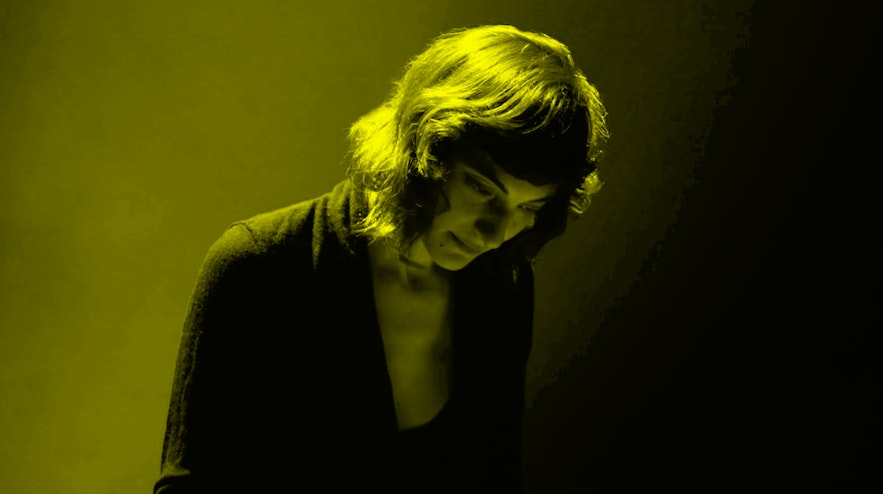 A person with shoulder-length brown hair and light skin looks down.