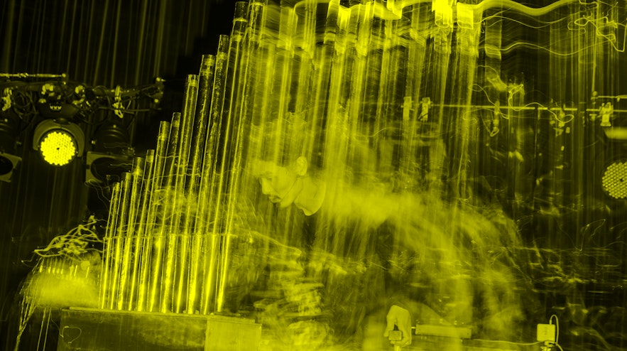 A long-exposure of a person with long black hair and light skin playing a pipe organ.