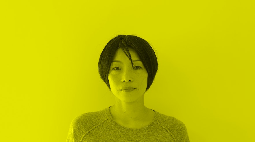 A person with short black hair and light skin gazes at you with a serious expression.