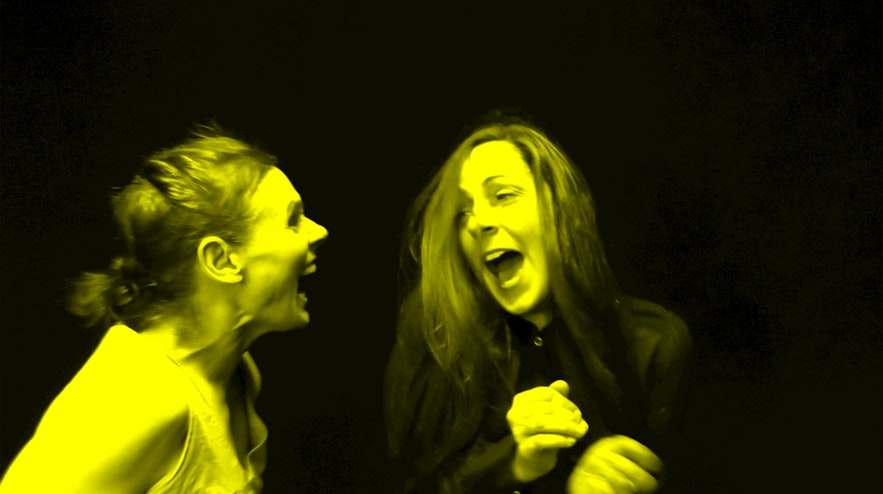 Two people standing next to each other laughing. The person on the left has reddish-brown hair and light skin, the person on the right has crimson and black ahri and light skin.