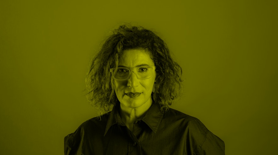 A person with dark, curly hair, glasses and light skin.
