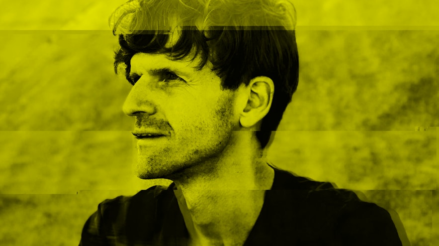 Person with dark hair and a beard, pictured from the waist up, looking away from the camera to the left