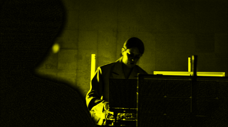 Person standing at a DJ deck in a dark room.