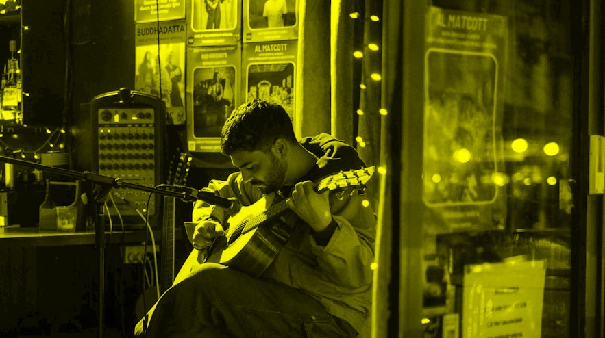 Person sitting on a stool playing an acoustic guitar