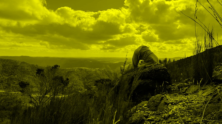 A person burying their head in the dirt on a mountain ridge.