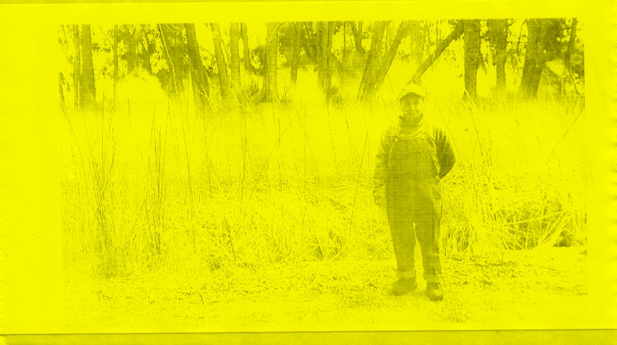 Person in a cap and overalls, standing in front of a field of tall grass.