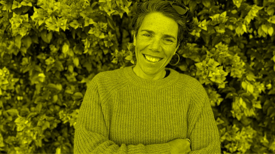 Person in purple sweater standing in front of greenery with purple flowers